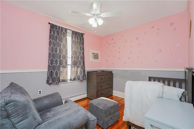 bedroom with a wall mounted air conditioner, wood-type flooring, baseboard heating, and ceiling fan