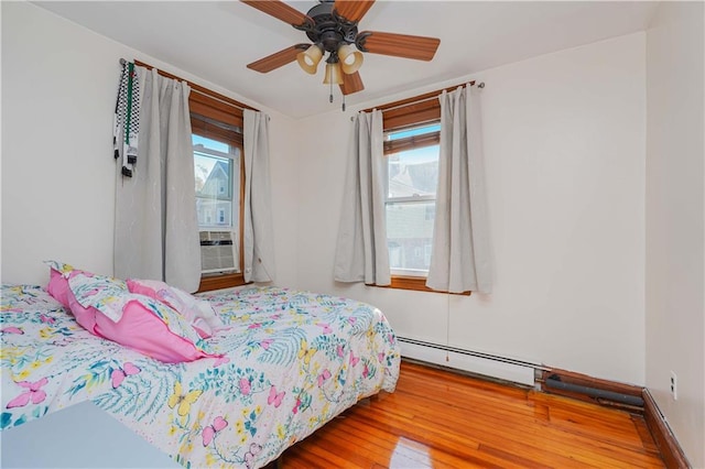 bedroom with baseboard heating, multiple windows, ceiling fan, and wood-type flooring