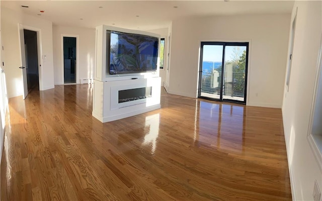 unfurnished living room featuring a baseboard radiator, baseboards, and wood finished floors