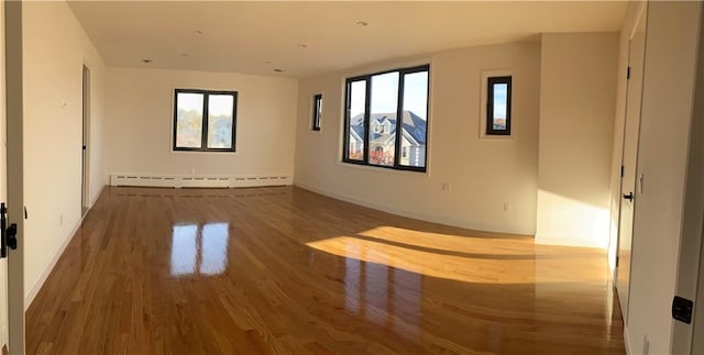 unfurnished room featuring wood finished floors, baseboards, and baseboard heating