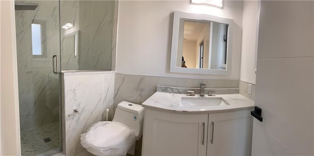 bathroom with a marble finish shower, vanity, tile walls, a wainscoted wall, and toilet