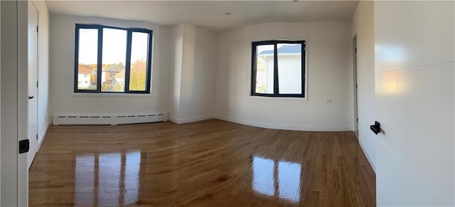 spare room featuring a baseboard heating unit, baseboards, and wood finished floors
