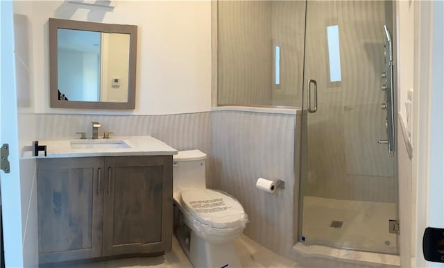 full bathroom featuring a wainscoted wall, vanity, a stall shower, and toilet