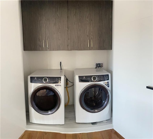 clothes washing area featuring washing machine and dryer, wood finished floors, and cabinet space