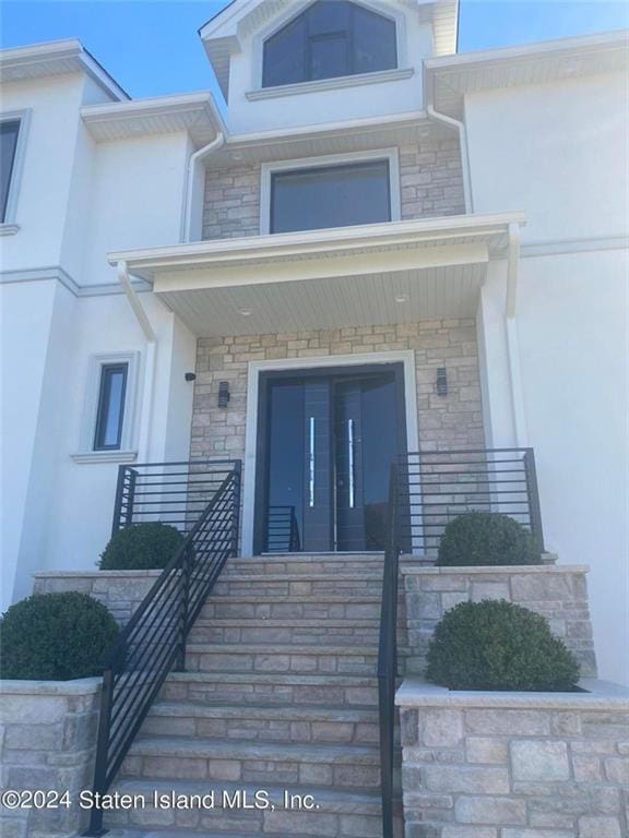 view of exterior entry with stucco siding, stone siding, and a porch