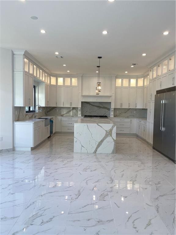 kitchen with built in refrigerator, backsplash, pendant lighting, and white cabinetry