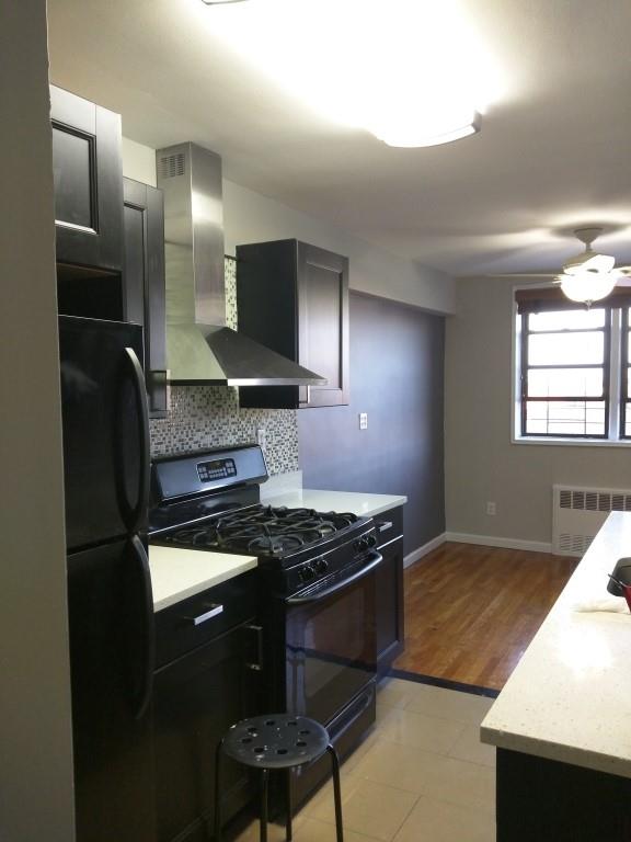 kitchen featuring radiator, decorative backsplash, ceiling fan, black appliances, and wall chimney exhaust hood