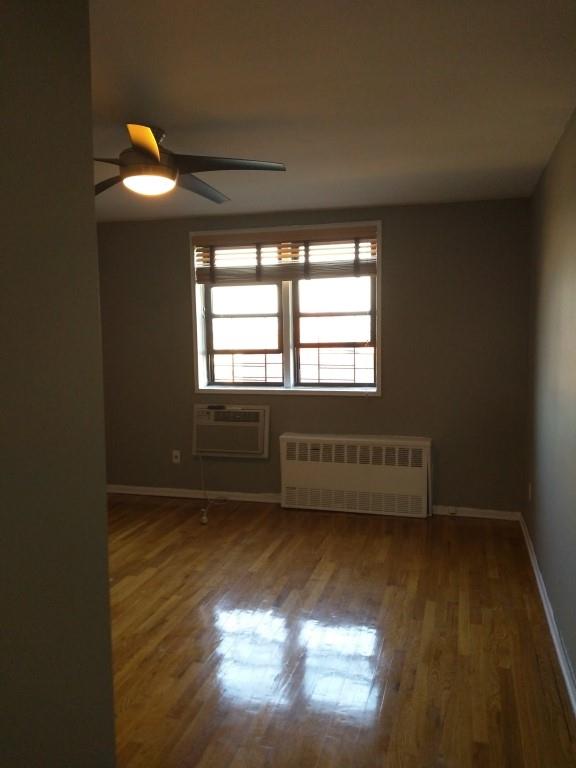 unfurnished room with ceiling fan, radiator heating unit, dark hardwood / wood-style floors, and a wall mounted air conditioner