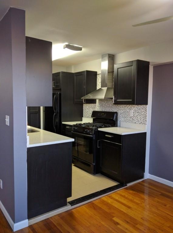 kitchen with tasteful backsplash, wall chimney exhaust hood, light hardwood / wood-style flooring, and black appliances