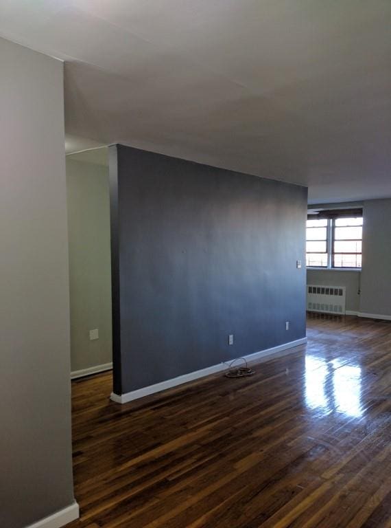 empty room with dark wood-type flooring and radiator heating unit