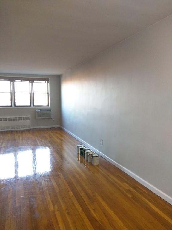 unfurnished room with radiator heating unit, hardwood / wood-style floors, and a wall unit AC