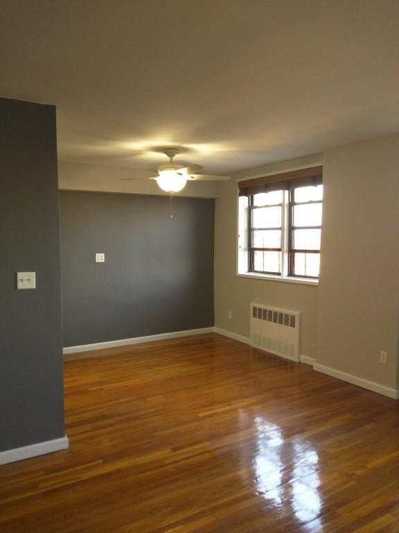 unfurnished room featuring dark wood-type flooring, radiator heating unit, and ceiling fan