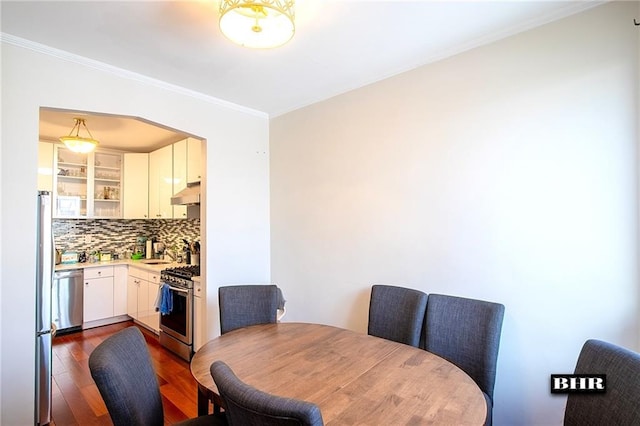 dining area with dark wood-type flooring, ornamental molding, and sink