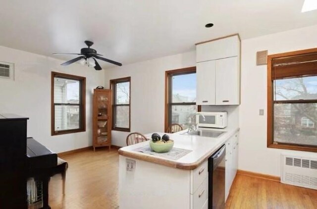 kitchen with stainless steel dishwasher, radiator heating unit, light hardwood / wood-style flooring, and white cabinets