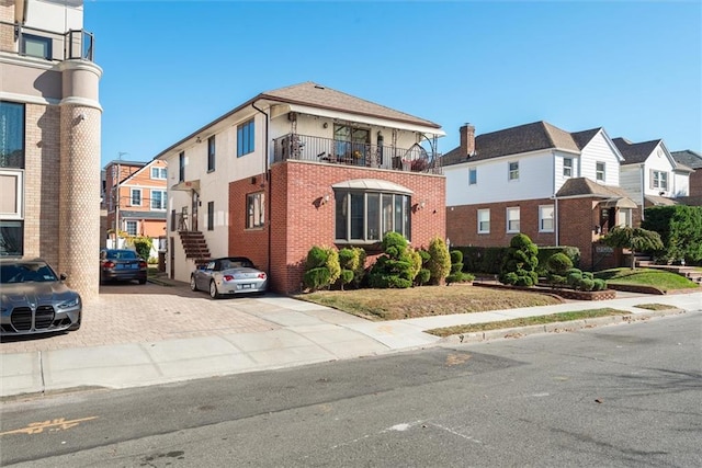 view of front of home with a balcony, a residential view, brick siding, and stairs