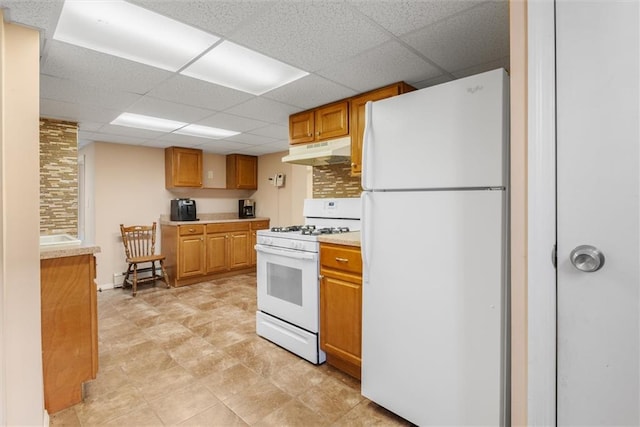 kitchen with white appliances, under cabinet range hood, a paneled ceiling, light countertops, and brown cabinetry