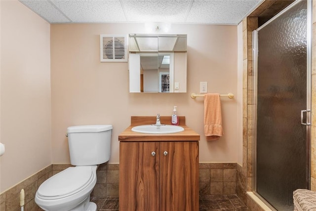 bathroom featuring a paneled ceiling, vanity, tile walls, toilet, and a shower with shower door