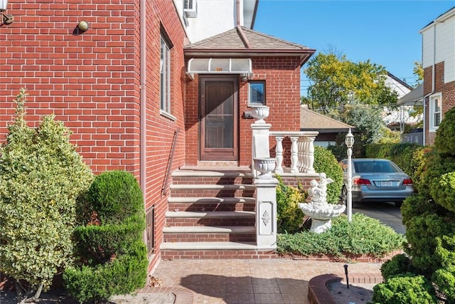 doorway to property with brick siding and a shingled roof