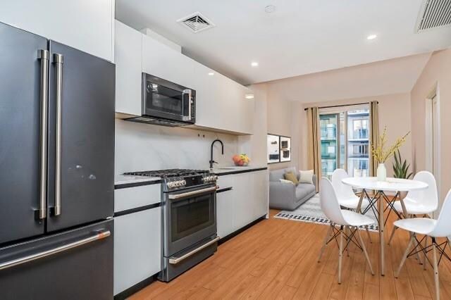 kitchen with appliances with stainless steel finishes, light wood-type flooring, white cabinetry, and sink