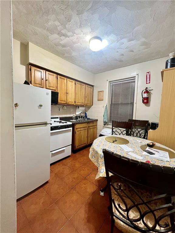 kitchen featuring dark countertops, a textured ceiling, brown cabinets, white appliances, and tile patterned flooring