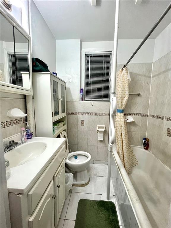 full bathroom with shower / tub combo with curtain, tile walls, vanity, tile patterned floors, and toilet