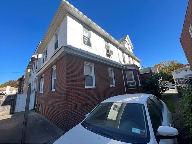 view of property exterior with cooling unit, brick siding, and fence