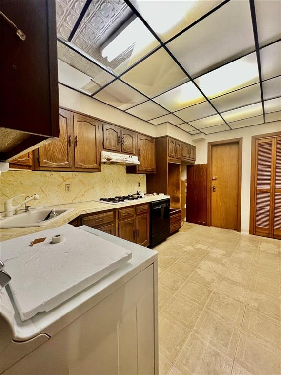 kitchen featuring black dishwasher, light floors, light countertops, a sink, and under cabinet range hood