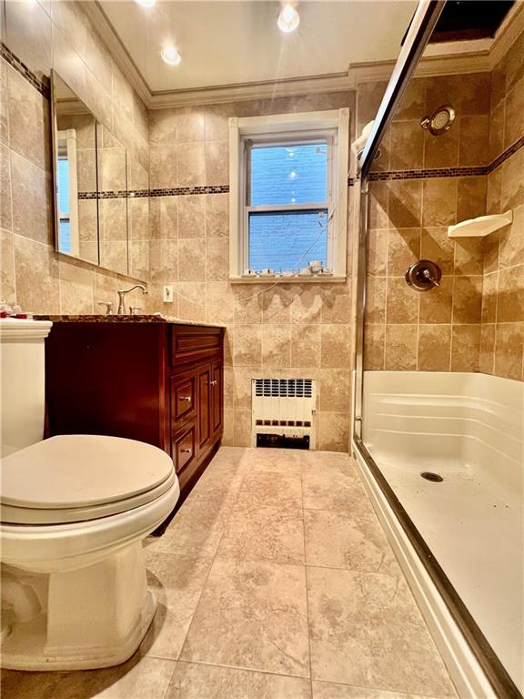 bathroom with toilet, tile walls, a tile shower, radiator heating unit, and vanity