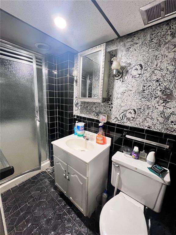 bathroom featuring toilet, tile walls, vanity, and walk in shower