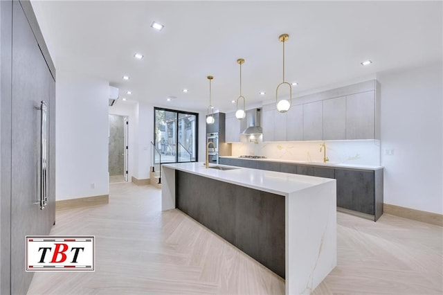 kitchen with wall chimney exhaust hood, a center island with sink, light parquet floors, and pendant lighting