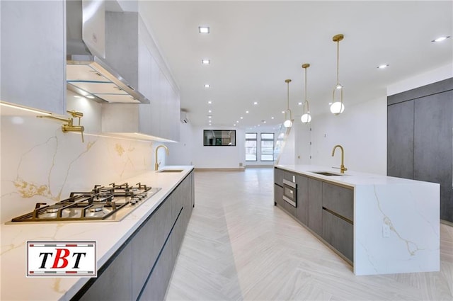 kitchen with wall chimney exhaust hood, light parquet floors, stainless steel gas cooktop, sink, and decorative light fixtures