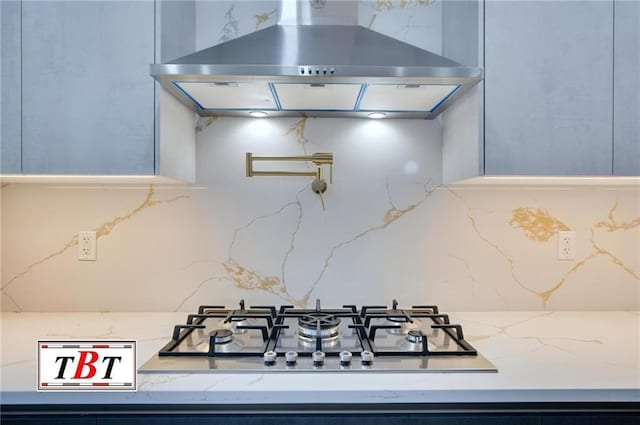 kitchen featuring tasteful backsplash, light stone countertops, wall chimney range hood, and stainless steel gas cooktop