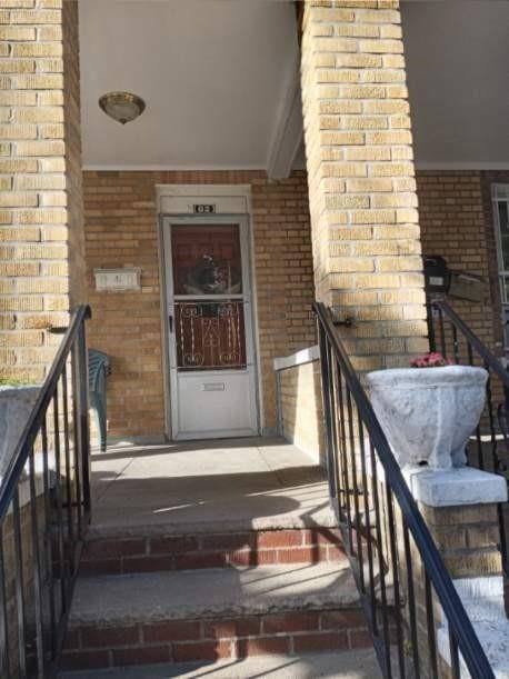 doorway to property with covered porch and brick siding