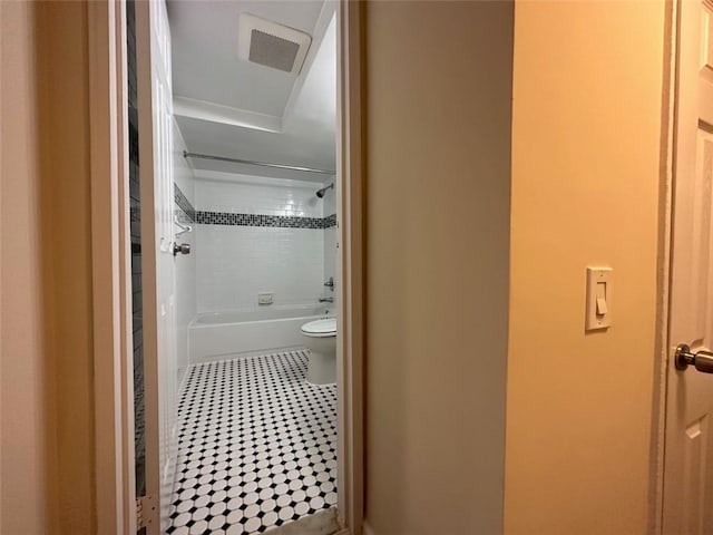 bathroom with tile patterned flooring, tiled shower / bath combo, and toilet