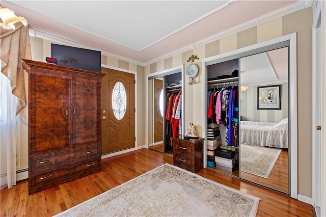 entrance foyer with a baseboard radiator, crown molding, baseboards, and wood finished floors