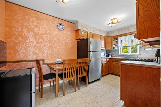 kitchen with stainless steel appliances, brown cabinets, light countertops, and wallpapered walls