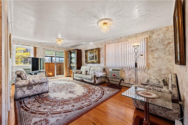 living area with wallpapered walls, wood finished floors, a wall mounted air conditioner, and a textured ceiling