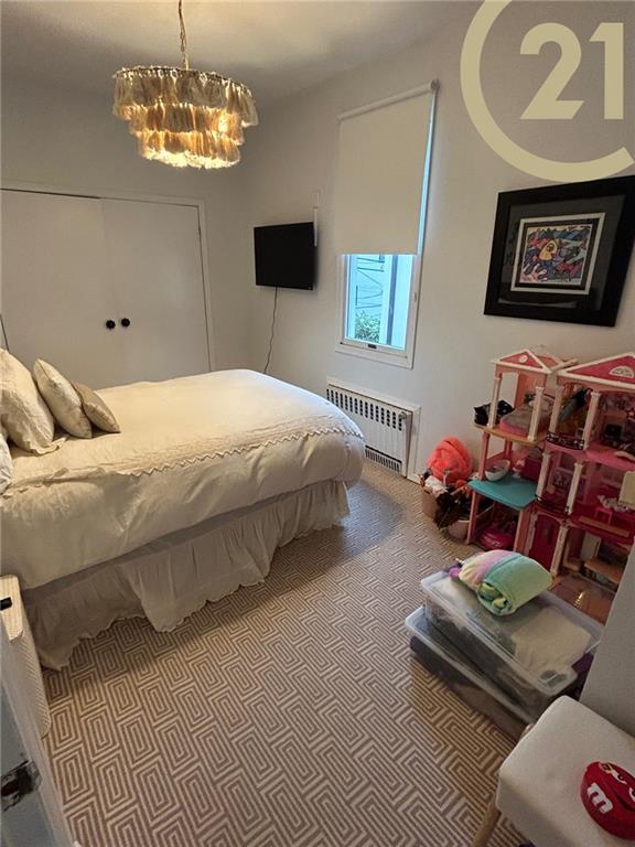 carpeted bedroom featuring radiator heating unit and an inviting chandelier