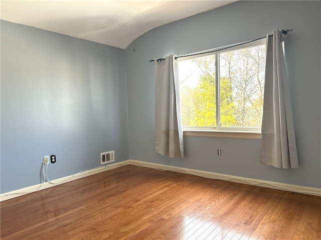 unfurnished room with visible vents, baseboards, and hardwood / wood-style flooring