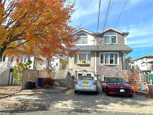 view of front of property with driveway, stone siding, stairs, and roof with shingles