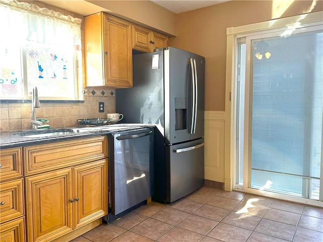 kitchen featuring light tile patterned floors, tasteful backsplash, dark countertops, appliances with stainless steel finishes, and a sink