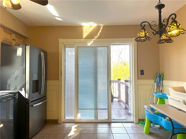 entryway with a wainscoted wall, ceiling fan with notable chandelier, light tile patterned flooring, and a decorative wall