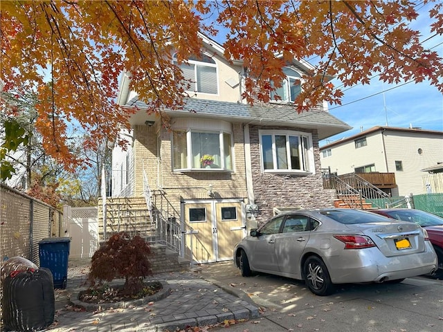 view of front facade with roof with shingles, brick siding, stairway, fence, and stone siding