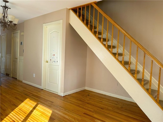 stairway with baseboards, wood finished floors, and a notable chandelier