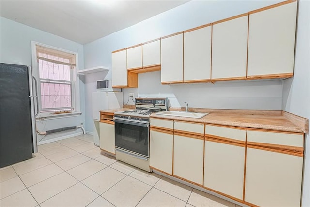 kitchen with stainless steel refrigerator, sink, white cabinets, light tile patterned floors, and white gas stove