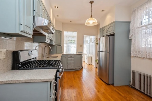 kitchen featuring sink, stainless steel fridge, radiator, gas range oven, and backsplash