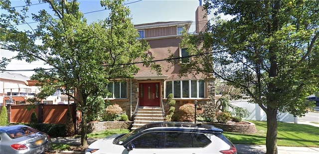 view of front facade featuring stucco siding, stone siding, and fence