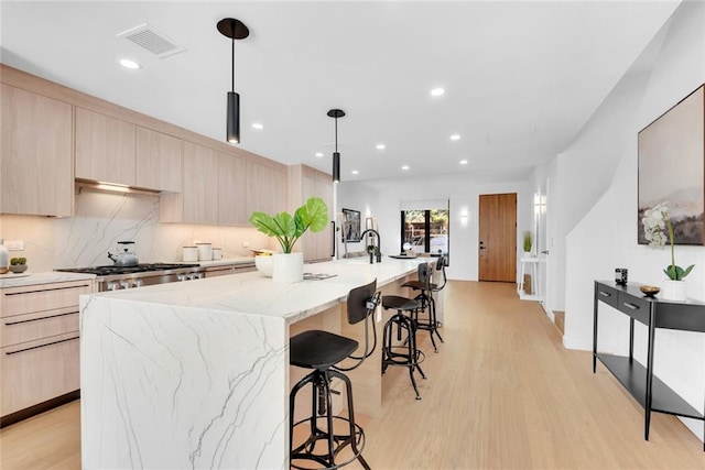 kitchen with a spacious island, light brown cabinets, decorative light fixtures, and light wood-type flooring