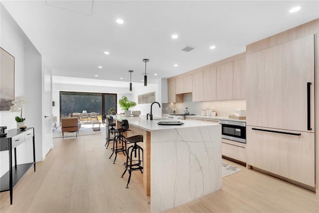 kitchen with an island with sink, pendant lighting, light hardwood / wood-style floors, and oven