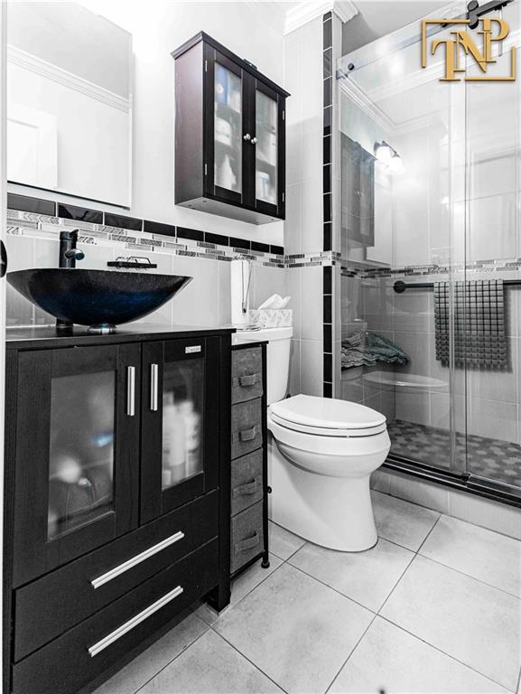 full bathroom with tile patterned flooring, toilet, tile walls, a shower stall, and ornamental molding